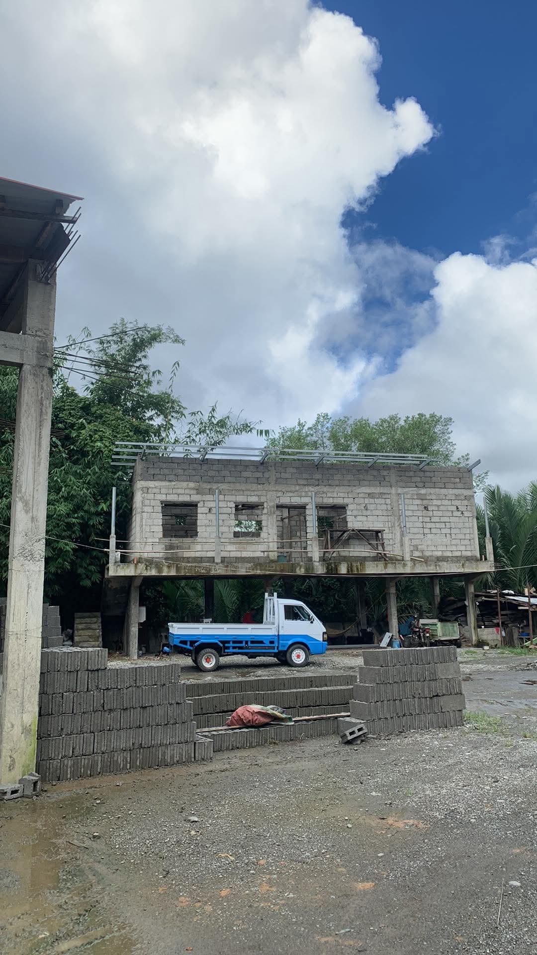 The house from across the lot, the elevated structure complete in blockwork and a pickup parked underneath